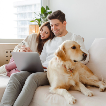 Couple smiling on couch with laptop next to white dog