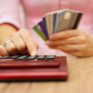 Person typing on calculator while holding stack of credit cards