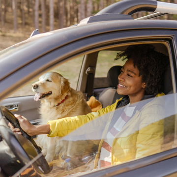 Lady driving car and smiling next to white dog in front seat