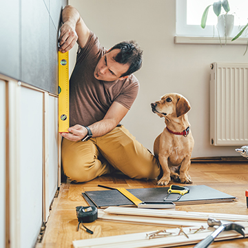 Man measuring wall in house next to curious dog